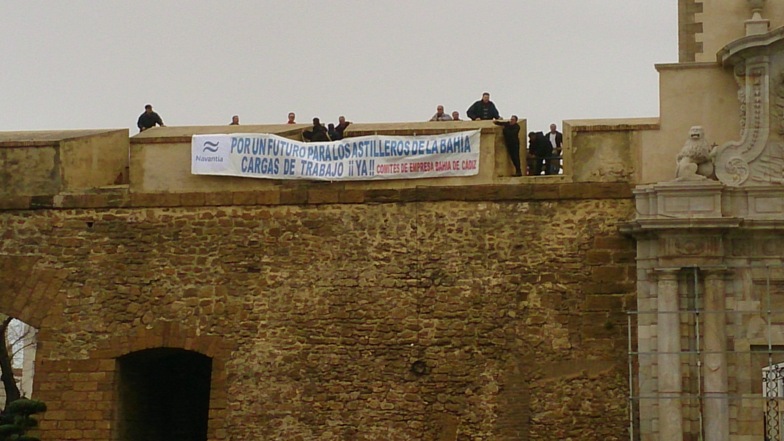 Empleados de Navantia colocan la pancarta en la muralla de Puerta Tierra